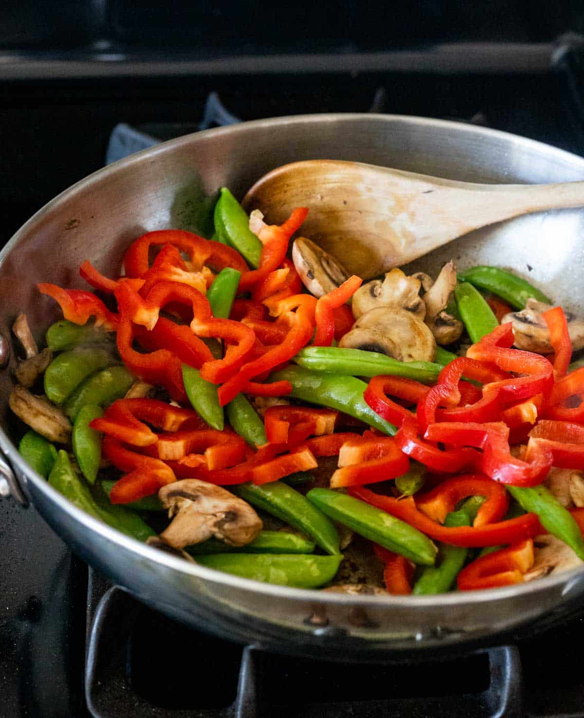 Mushrooms, peppers and sugar snap peas sautéing in a skillet on the stovetop.