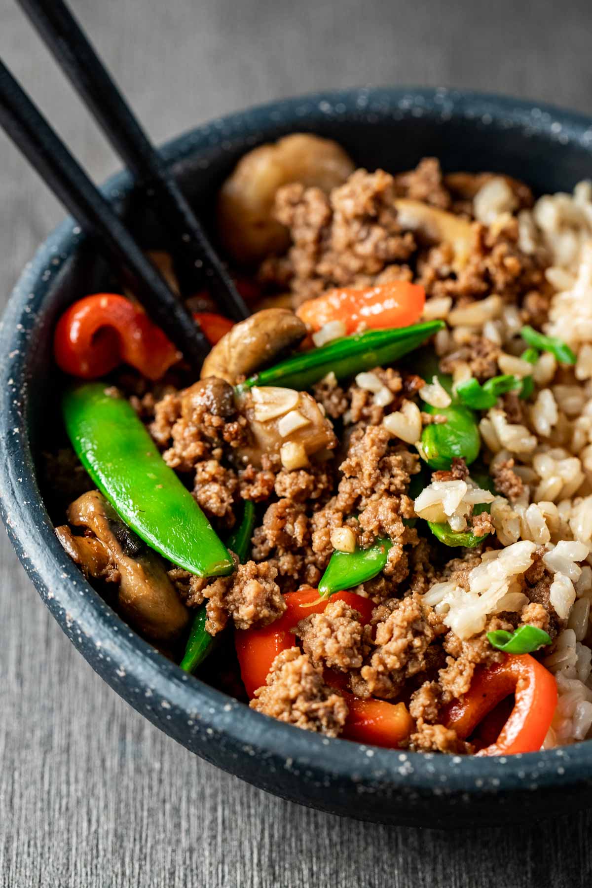 Side view of ground beef stir fry in a bowl with chopsticks inserted into it.