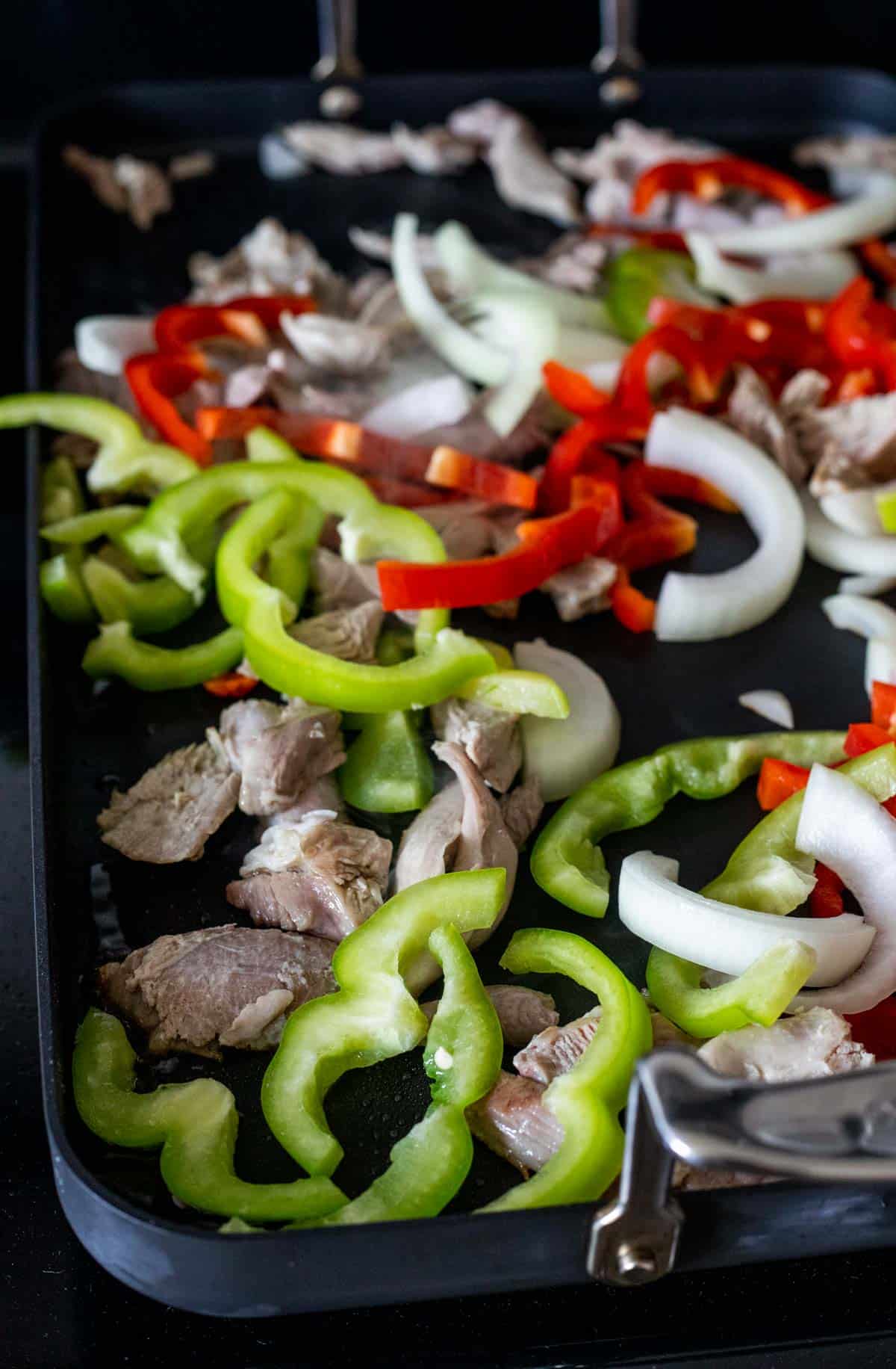 Raw slices of pepper and onion arranged on a pan with shredded leftover turkey.