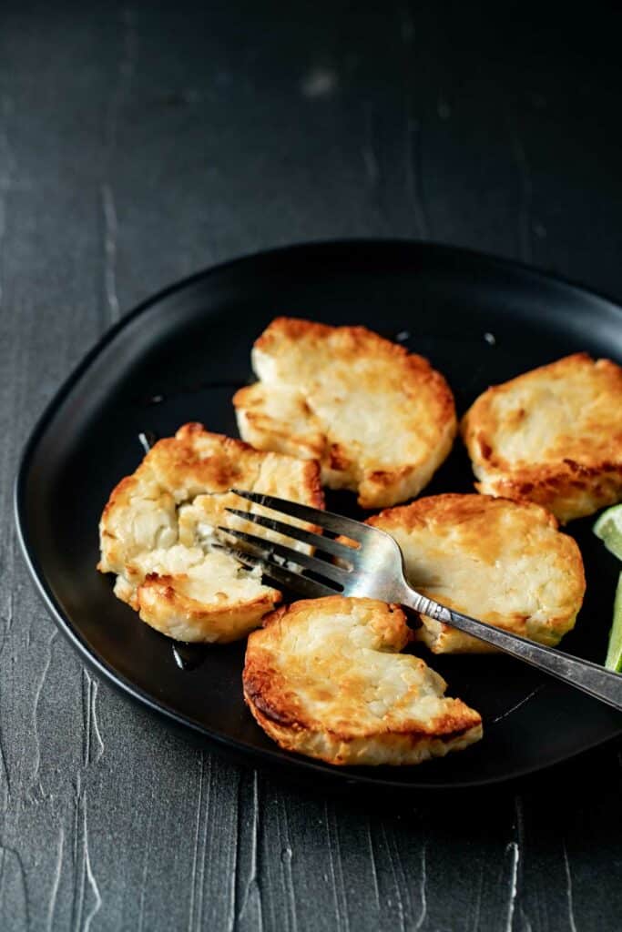 A close up view of air fried halloumi cheese on a black plate with a fork.