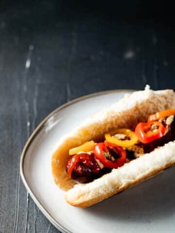 view of a sausage link on a white bun with red and yellow peppers