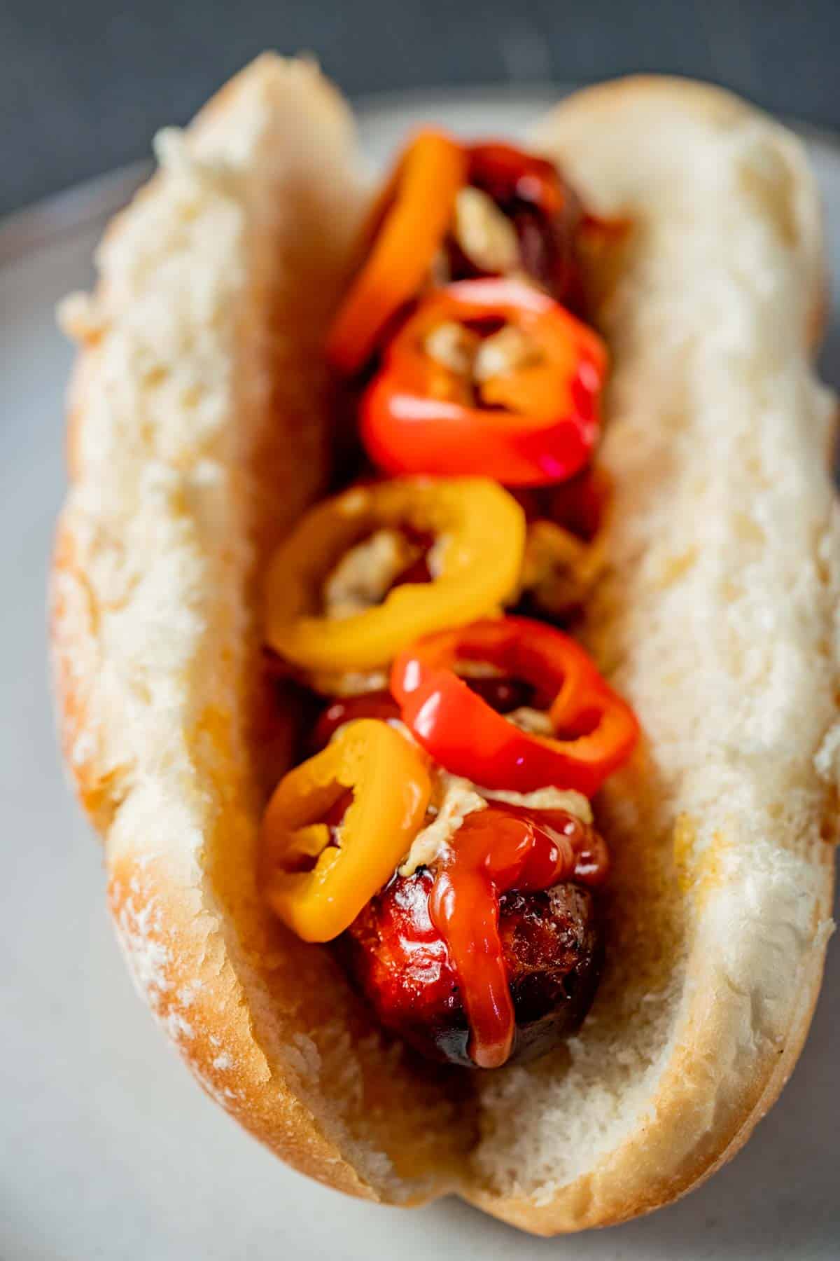 view of a sausage link on a white hot dog bun with yellow and red peppers