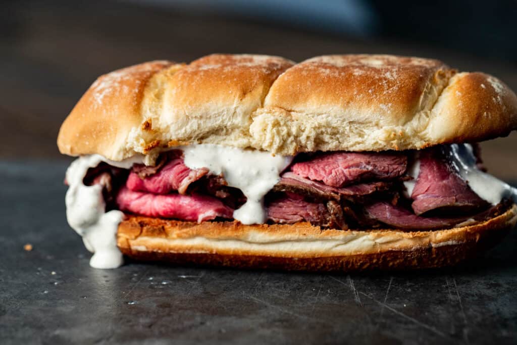 super close up view of a roast beef sandwich with white sauce on a black surface