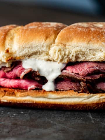 super close up view of a roast beef sandwich with white sauce on a black surface