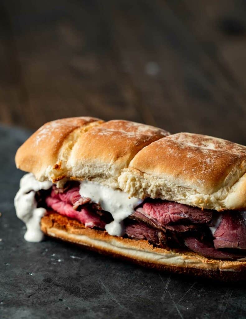 close up view of a Roast Beef sandwich with white sauce on a black surface