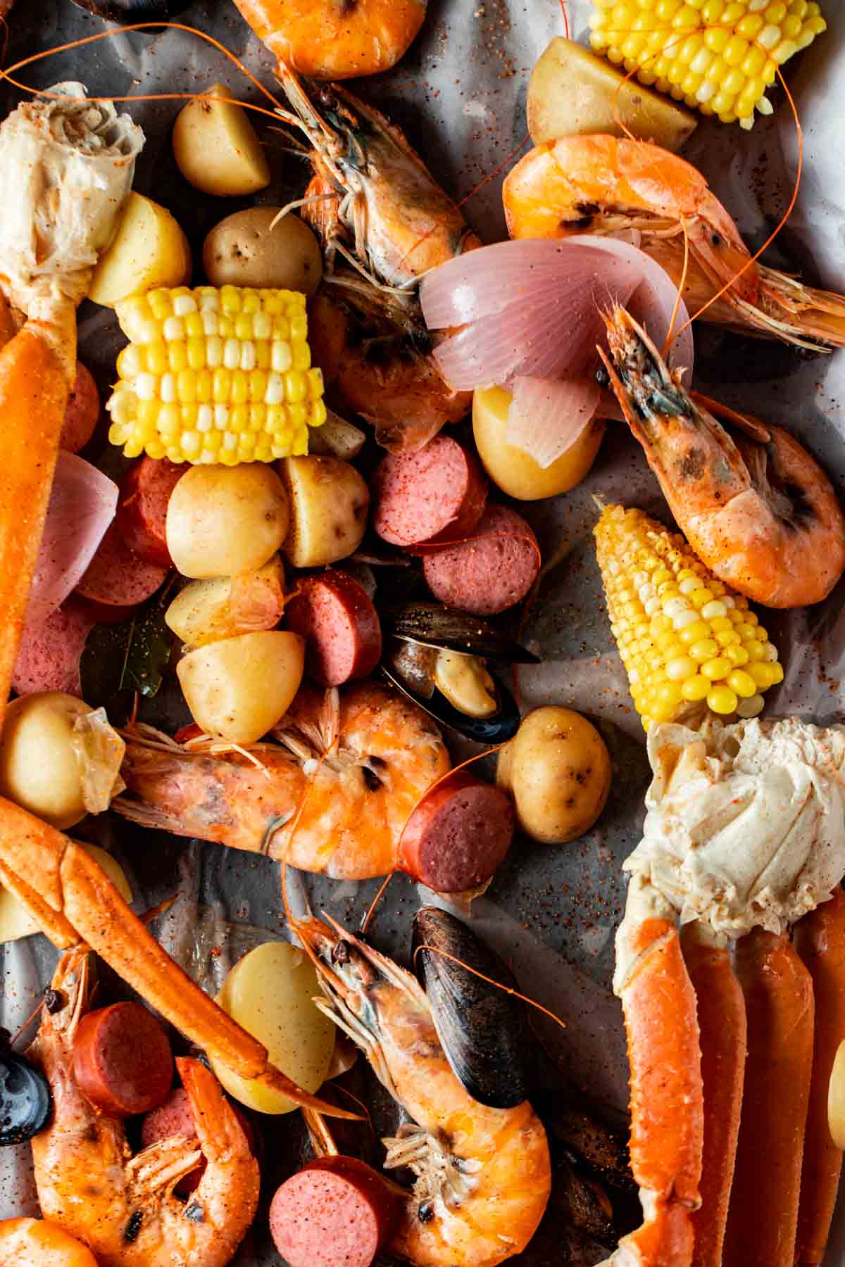 shellfish, sausage, corn and potatoes spread out on a table over brown paper