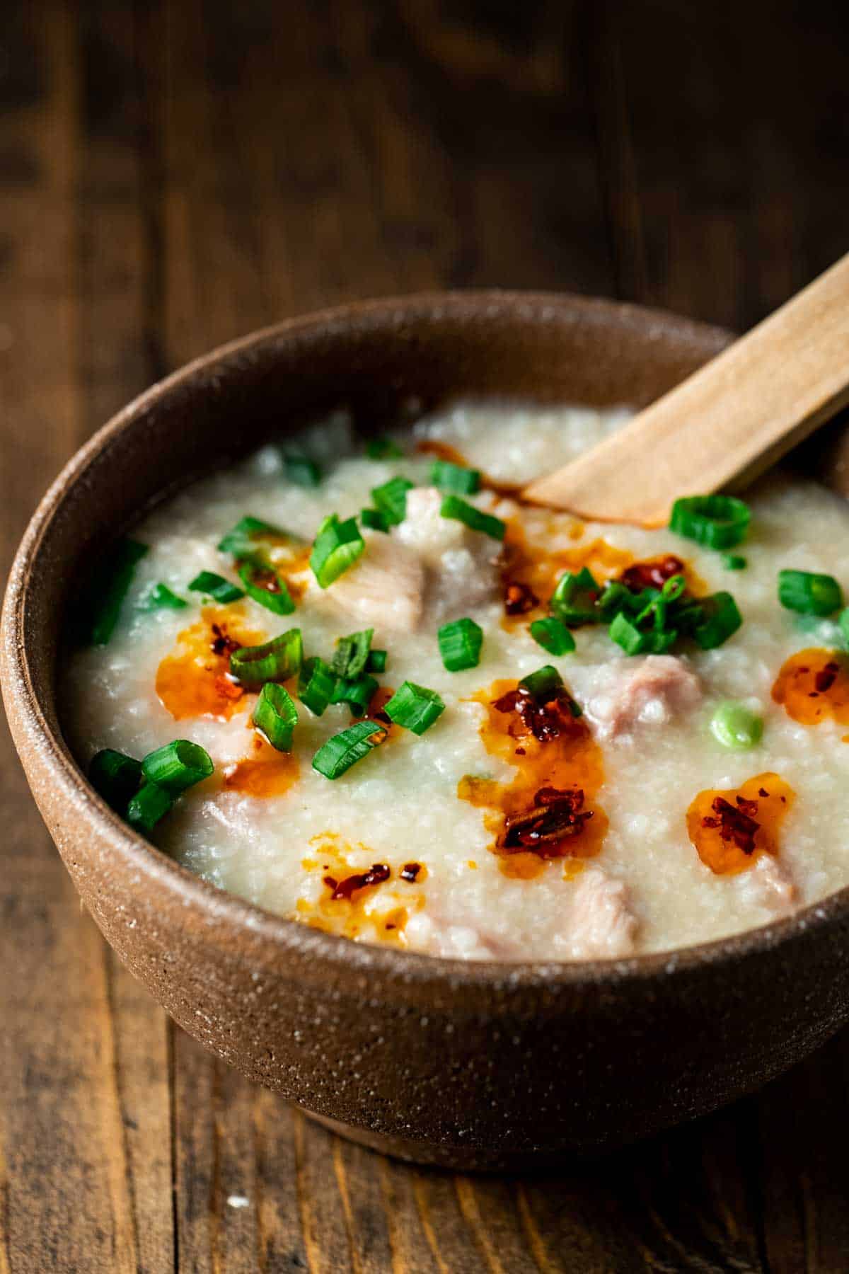 a bowl of congee with green onions and chili oil on it