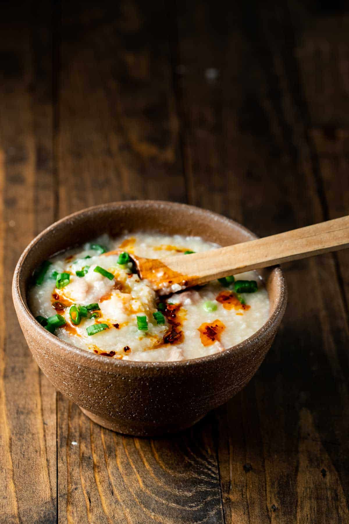a spoonful of congee over a bowl of it garnished with green onions and chili oil