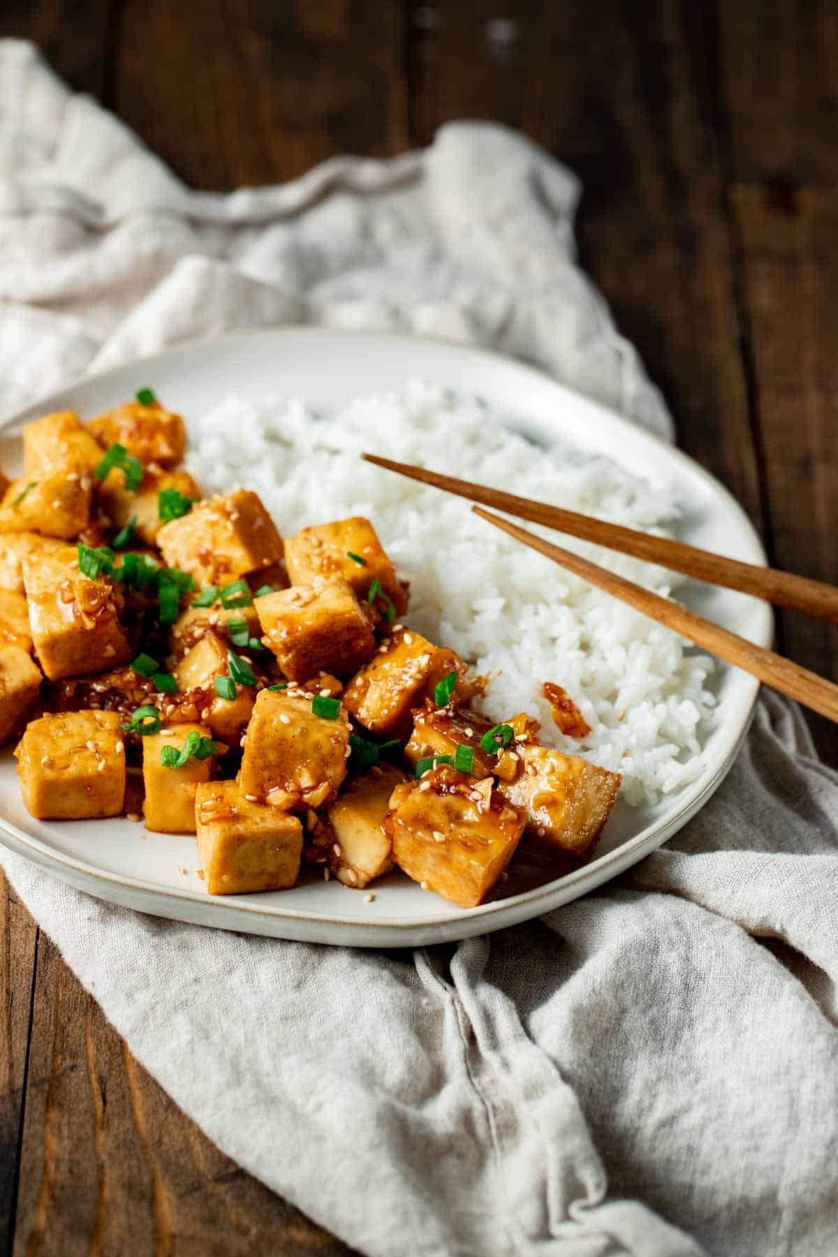 honey garlic tofu with rice on a white on a plate with chopsticks