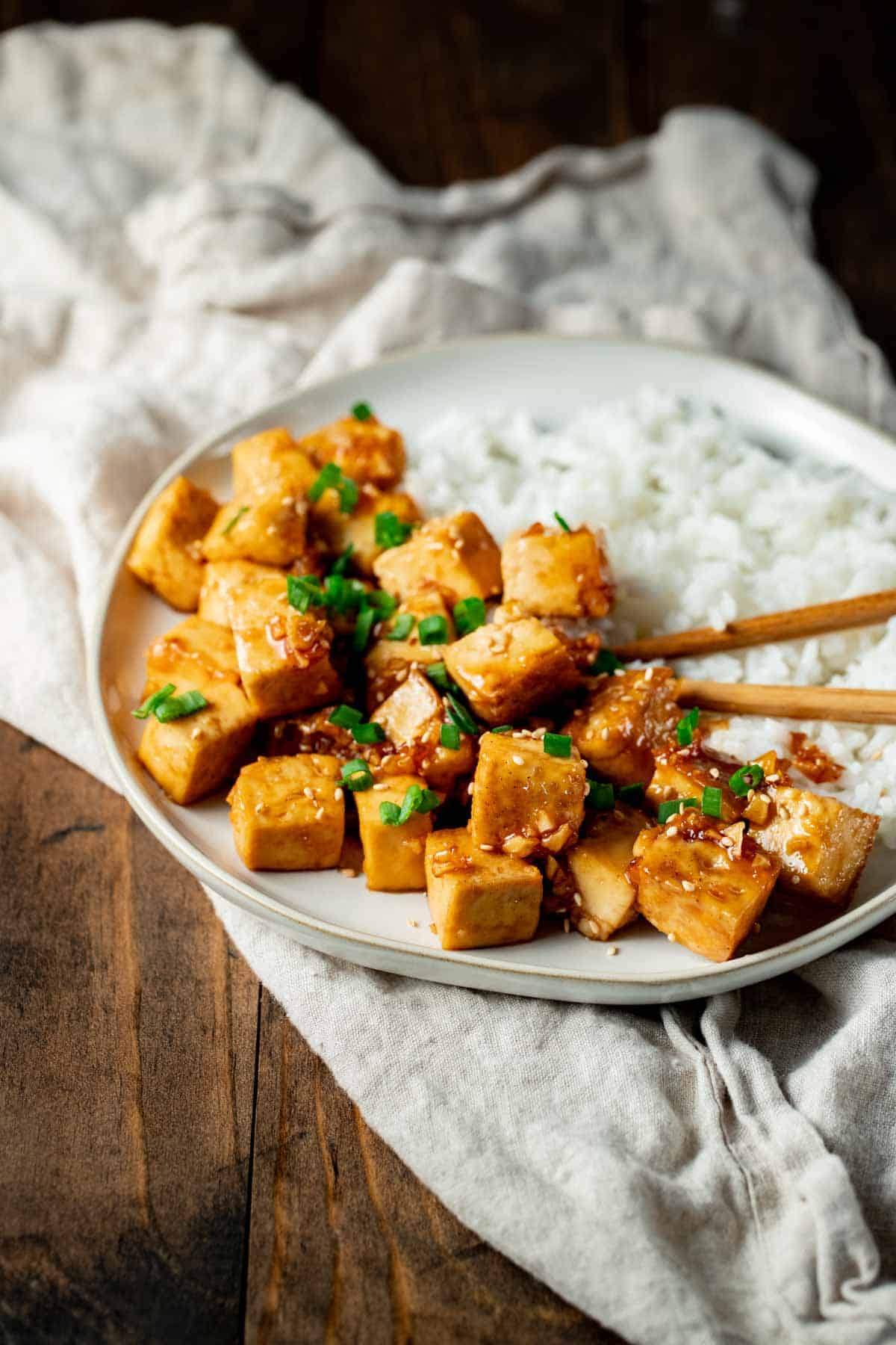 up close view of tofu and rice on a white plate with chop sticks
