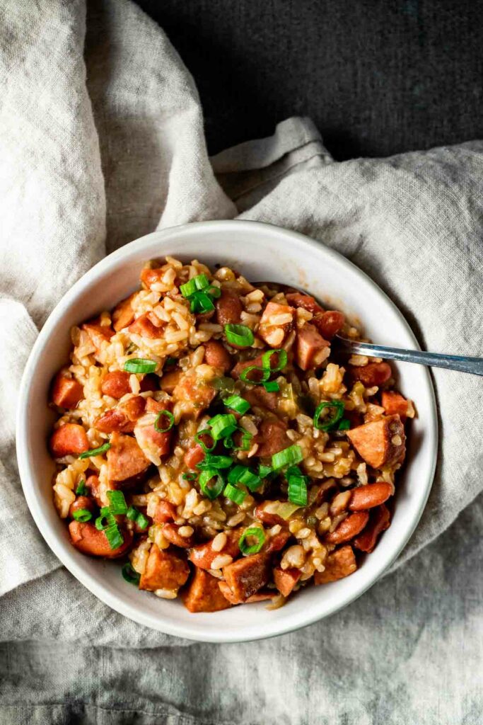 view of red beans and rice with scallions on top in a white bowl with a silver spoon