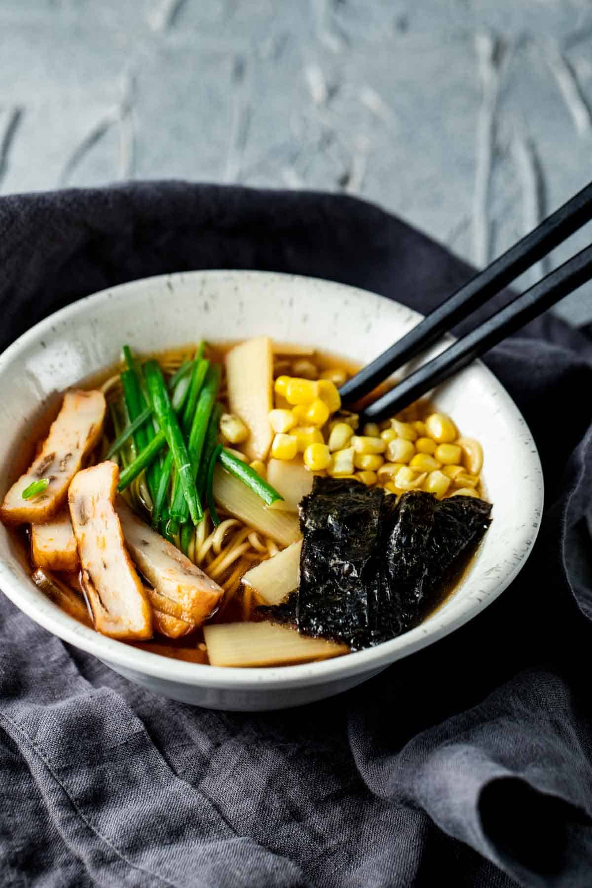 a bowl of broth with corn, seaweed, green onions and noodles in it