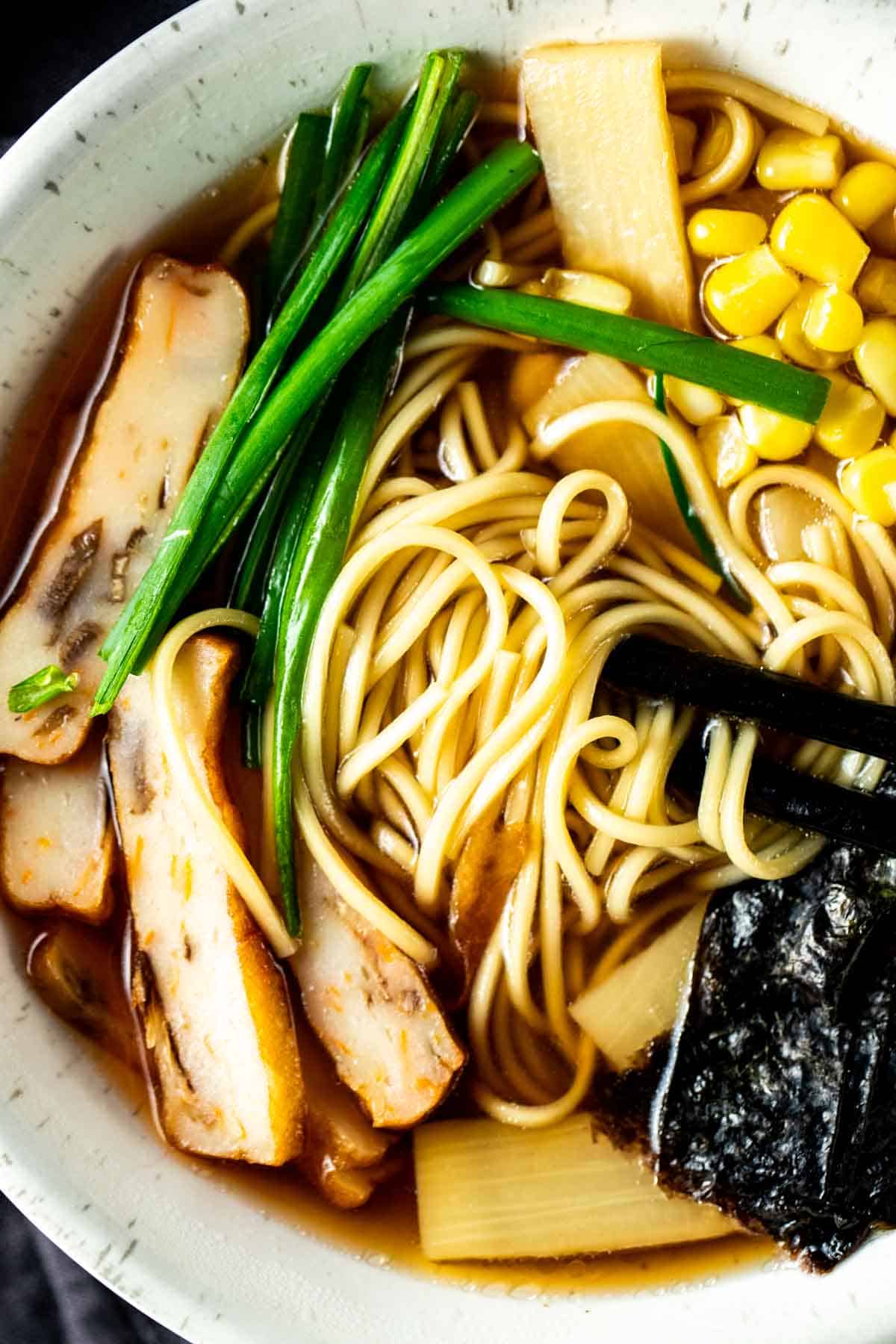 chopsticks with noodles wrapped around in a bowl of broth and vegetables