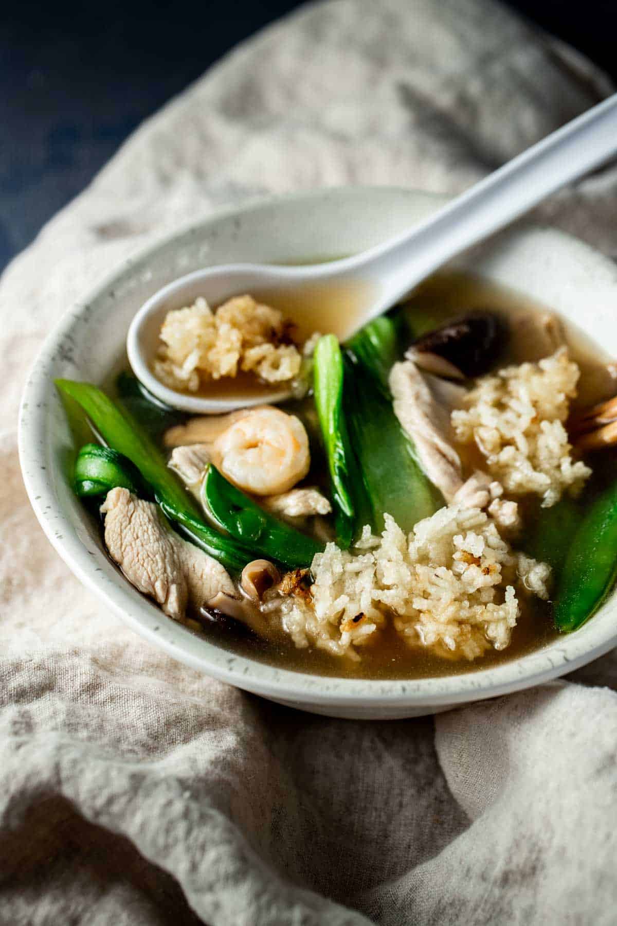 a bowl of soup with green vegetables, crispy rice and shrimp with a spoon in it