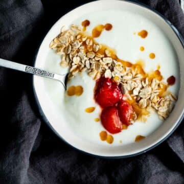 yogurt topped with granola and strawberries in a bowl with a spoon