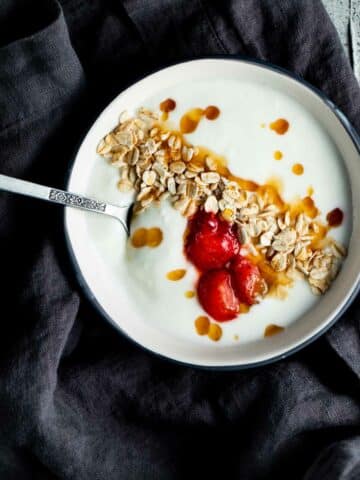 yogurt topped with granola and strawberries in a bowl with a spoon