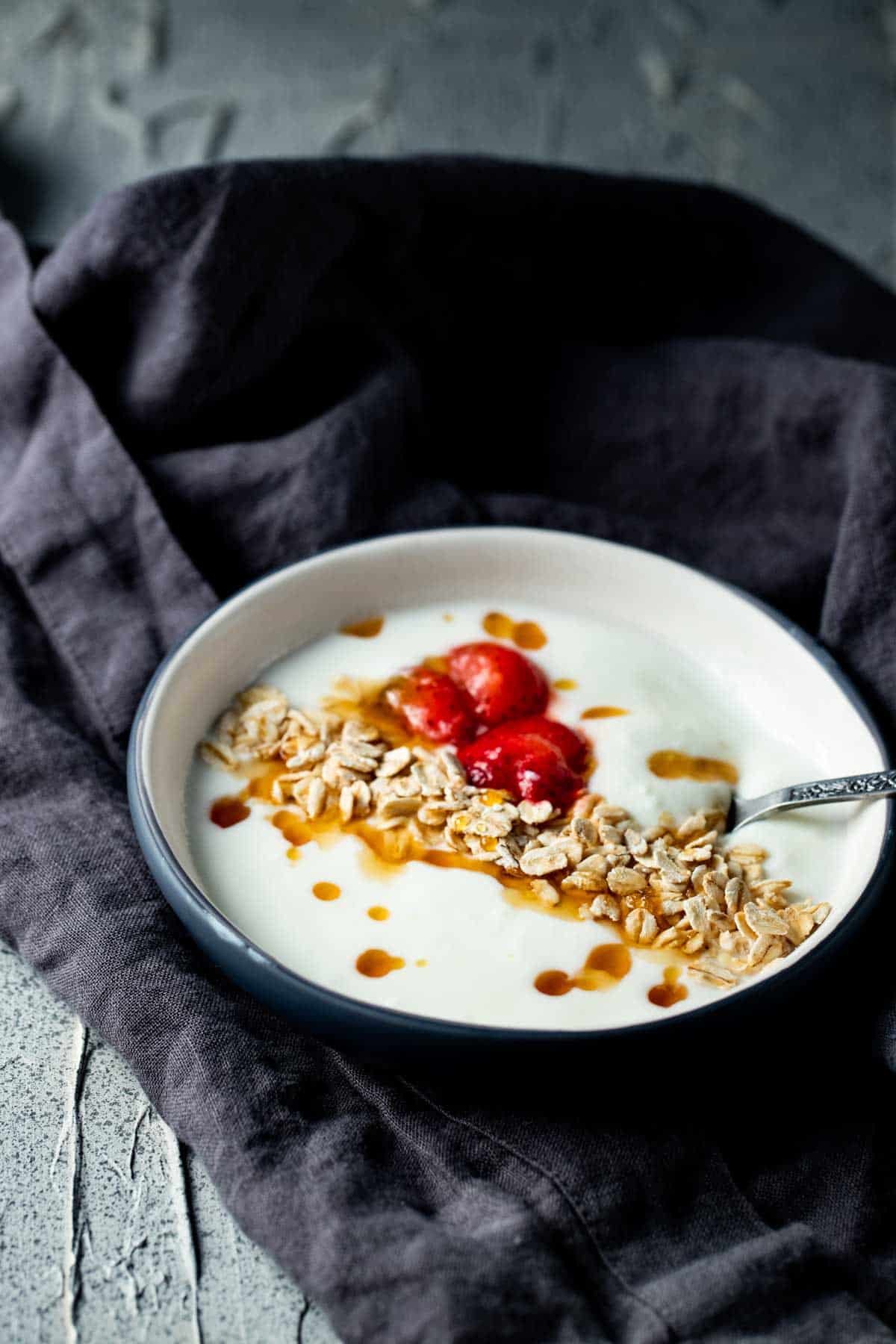 Side view of a bowl of yogurt topped with berries, honey and granola