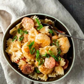 a bowl of creamy pasta with shrimp and sausage and a spoon in it