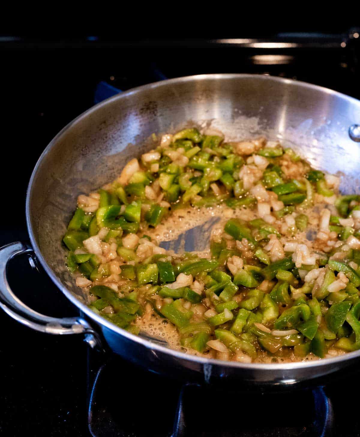 green pepper and onions cooking in a roux in a skillet