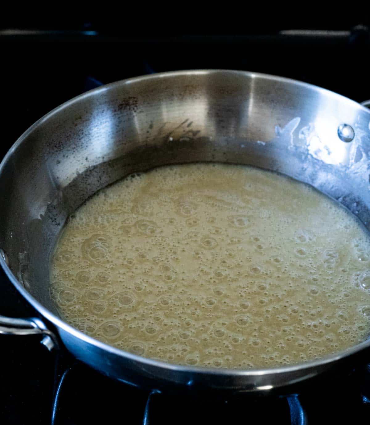 a yellow colored liquid cooking in a skillet (roux)