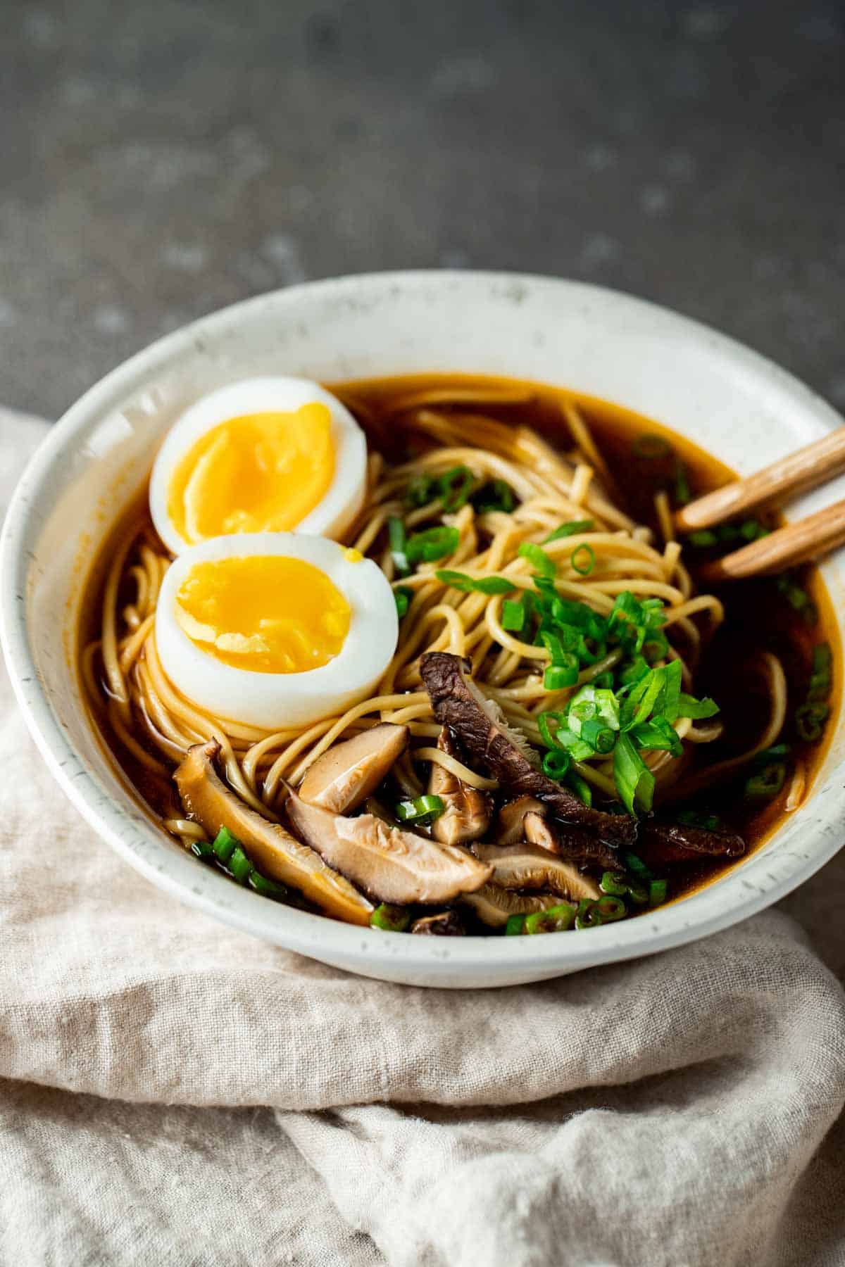 a bowl of ramen topped with eggs, mushrooms and green onions with chopsticks
