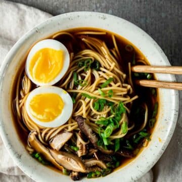 soup with noodles, green onions, halved boiled eggs, sliced mushrooms and chopsticks in it