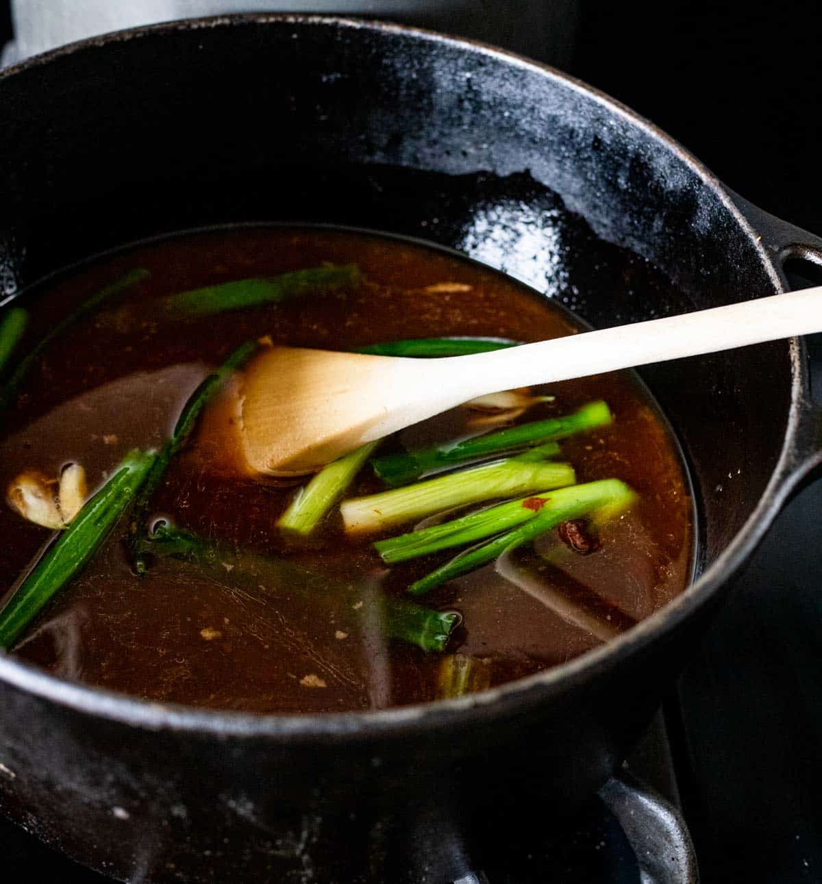 dark broth and green onions in a large black pot