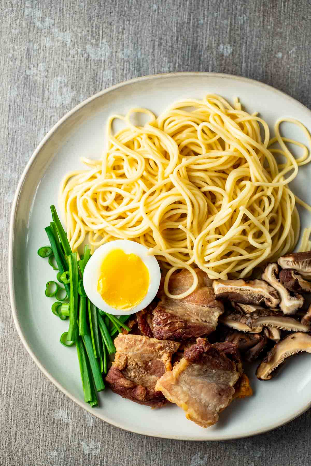 a plate of noodles and pork belly with a halved egg and green onions