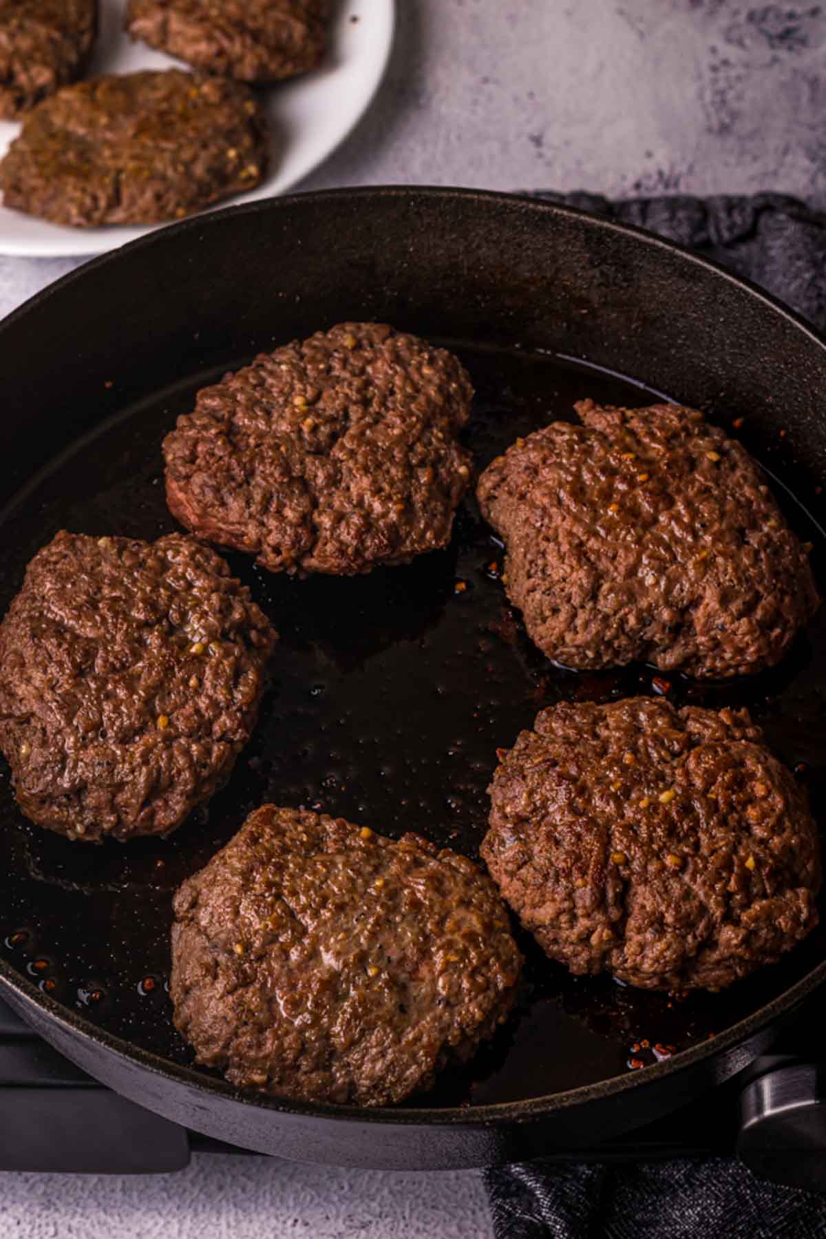 cooked hamburgers being seared in a skillet