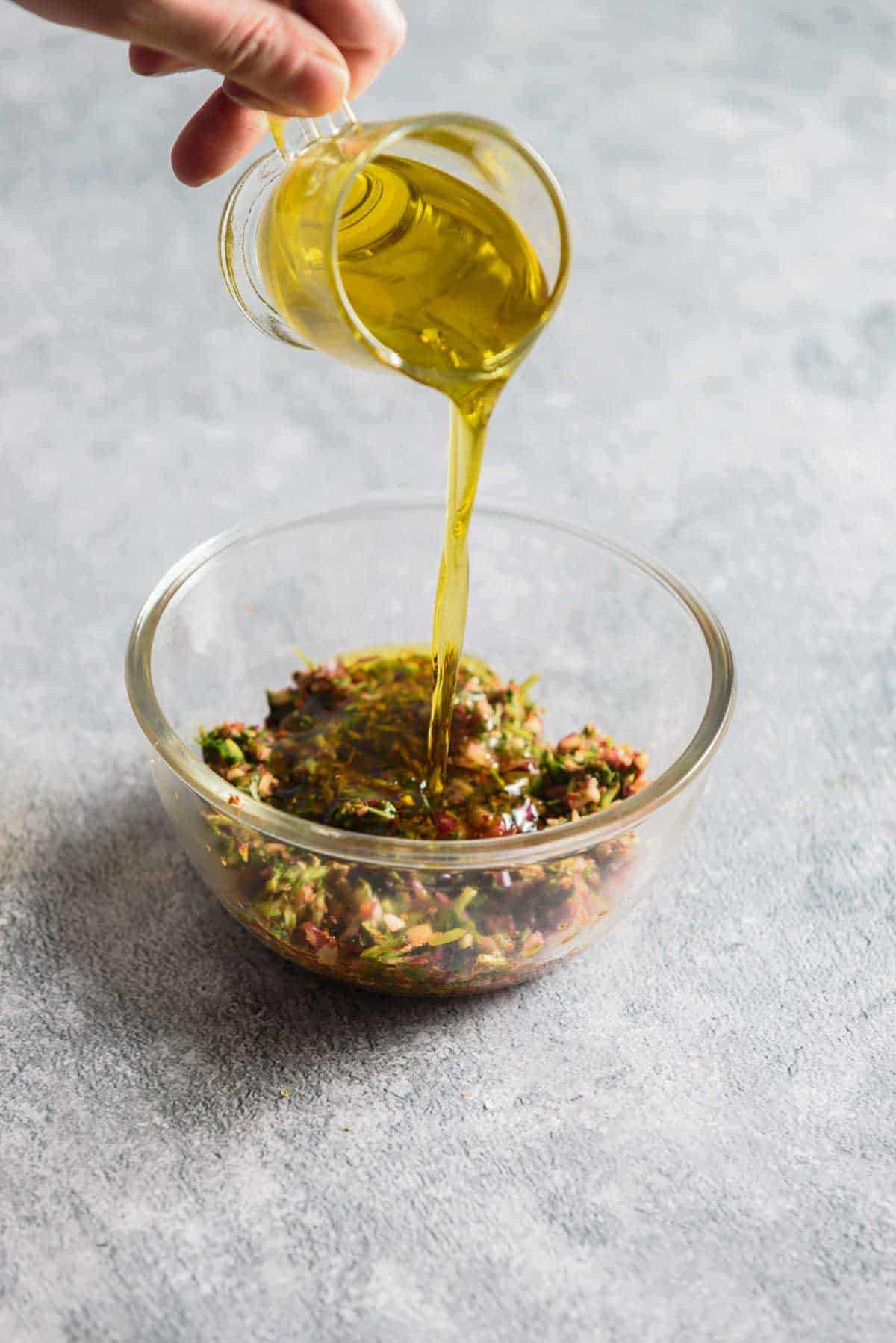 olive oil being poured into a bowl with herbs and spices
