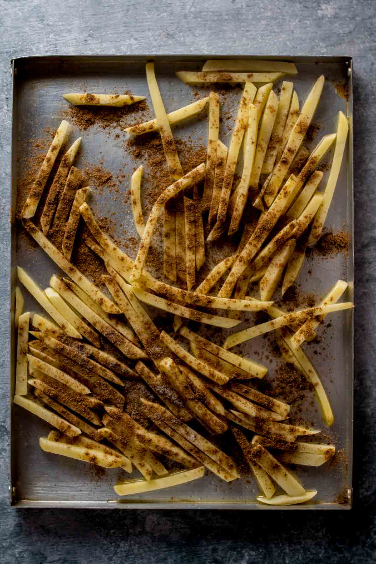 raw french fries covered in seasoning on a baking sheet