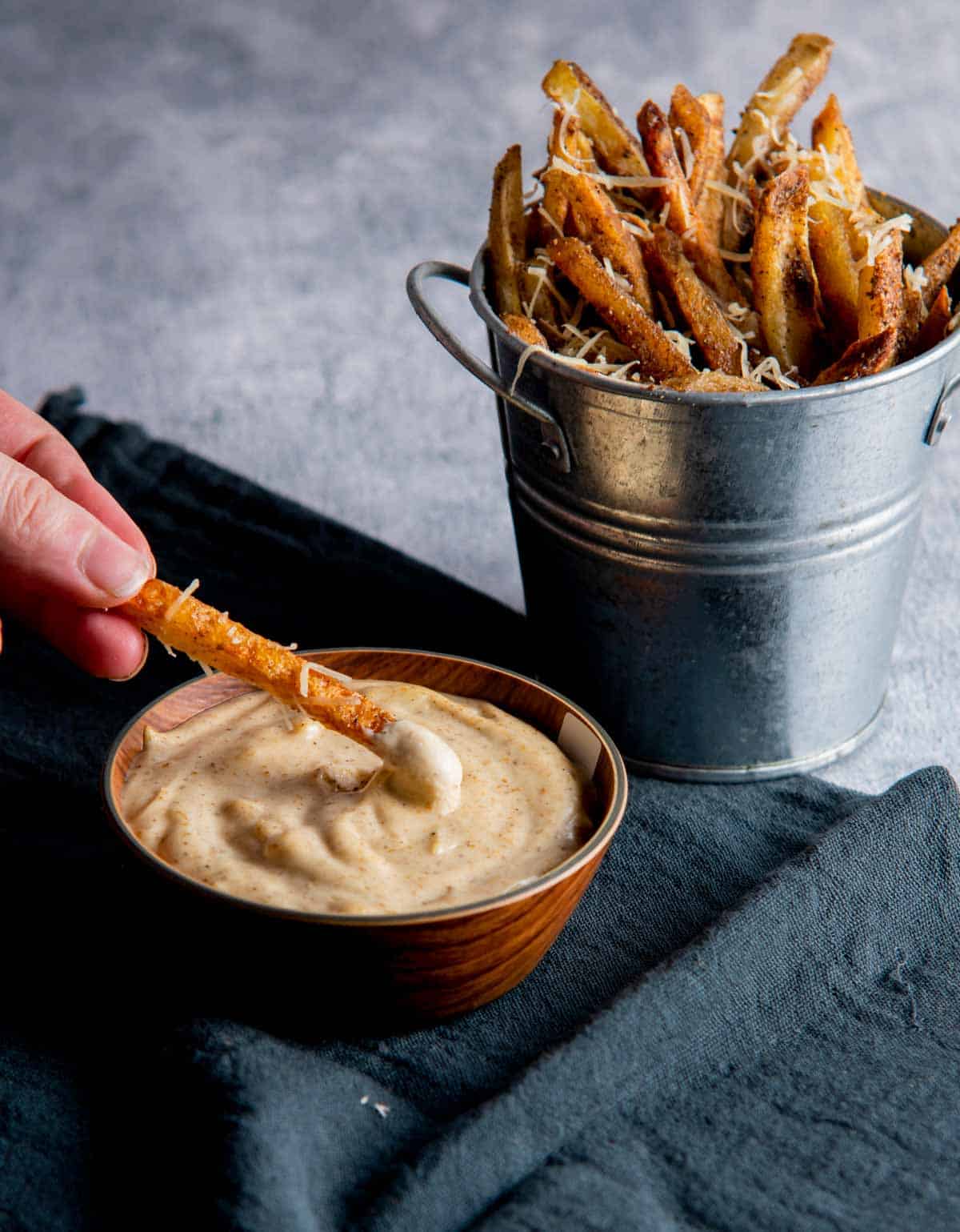 a hand dipping a fry in the truffle mayonnaise