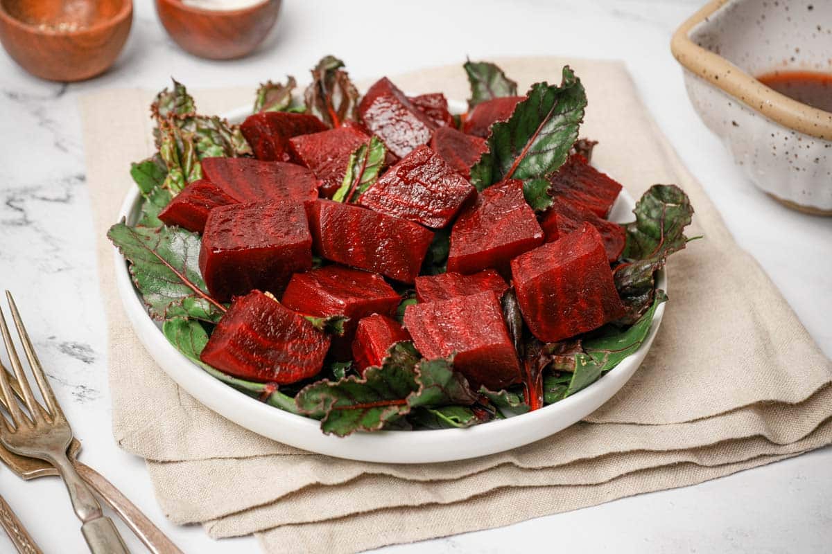 cooked and cut beets on a plate of salad green