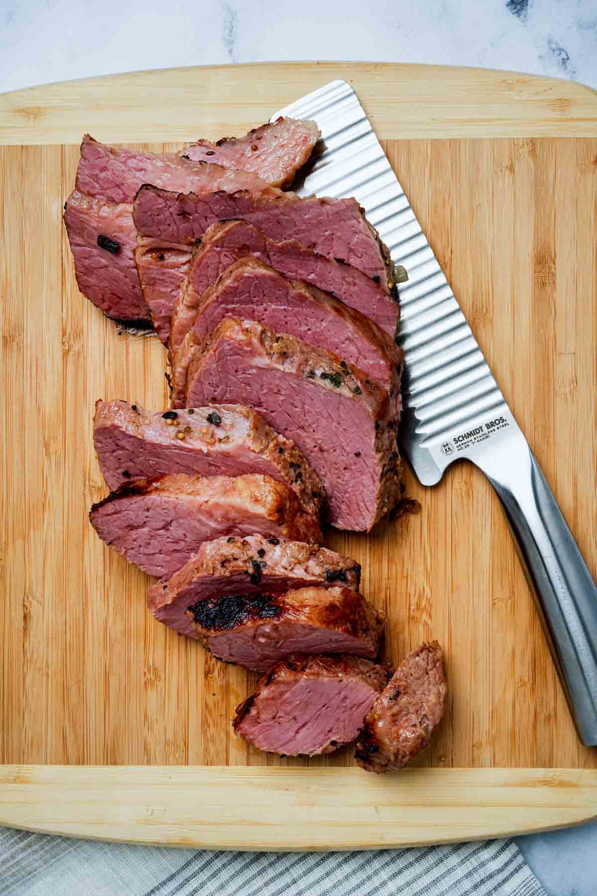 Corned beef being sliced on a wood cutting board