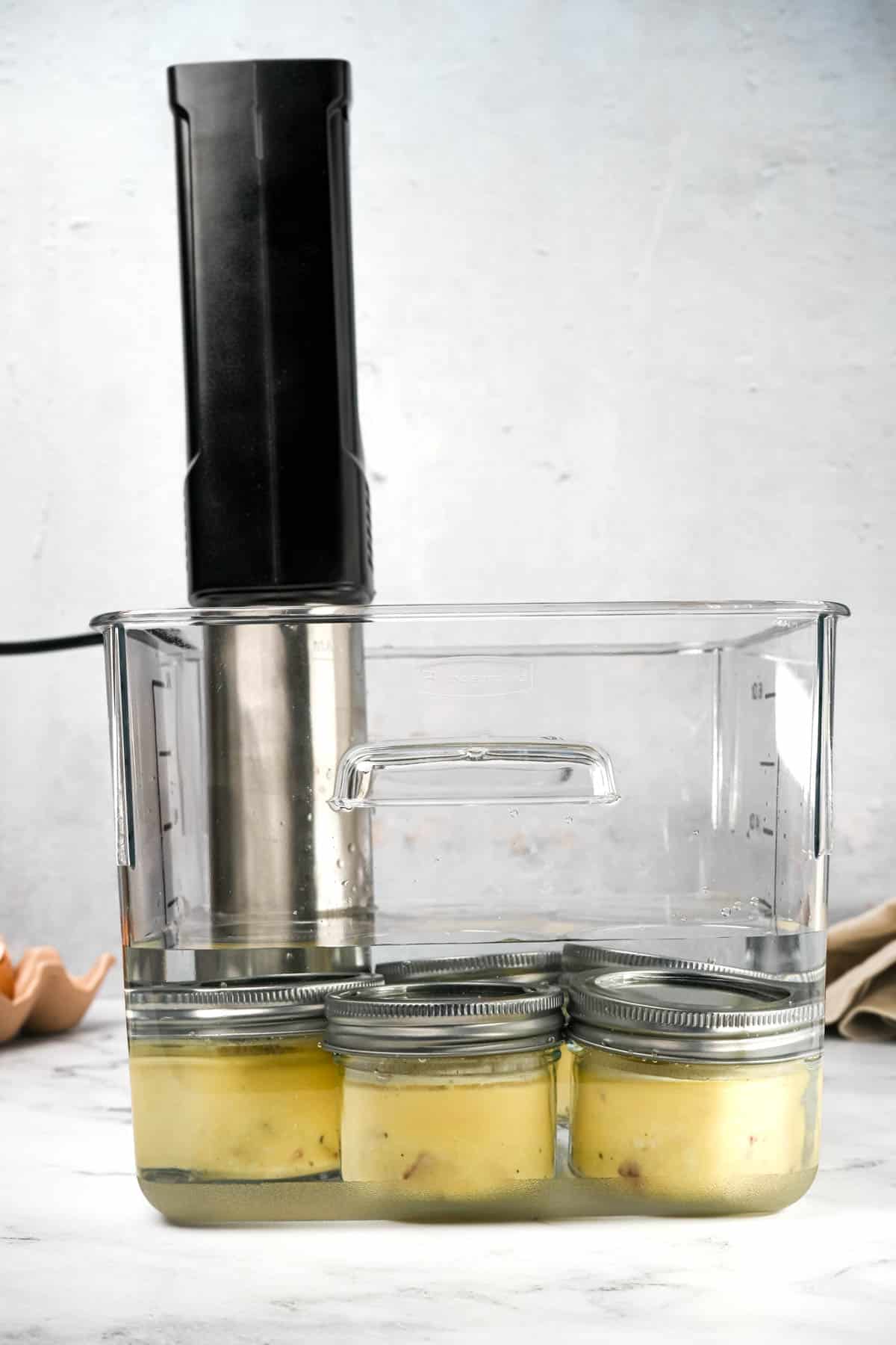 glass jars with yellow liquid sitting in a sous vide water bath