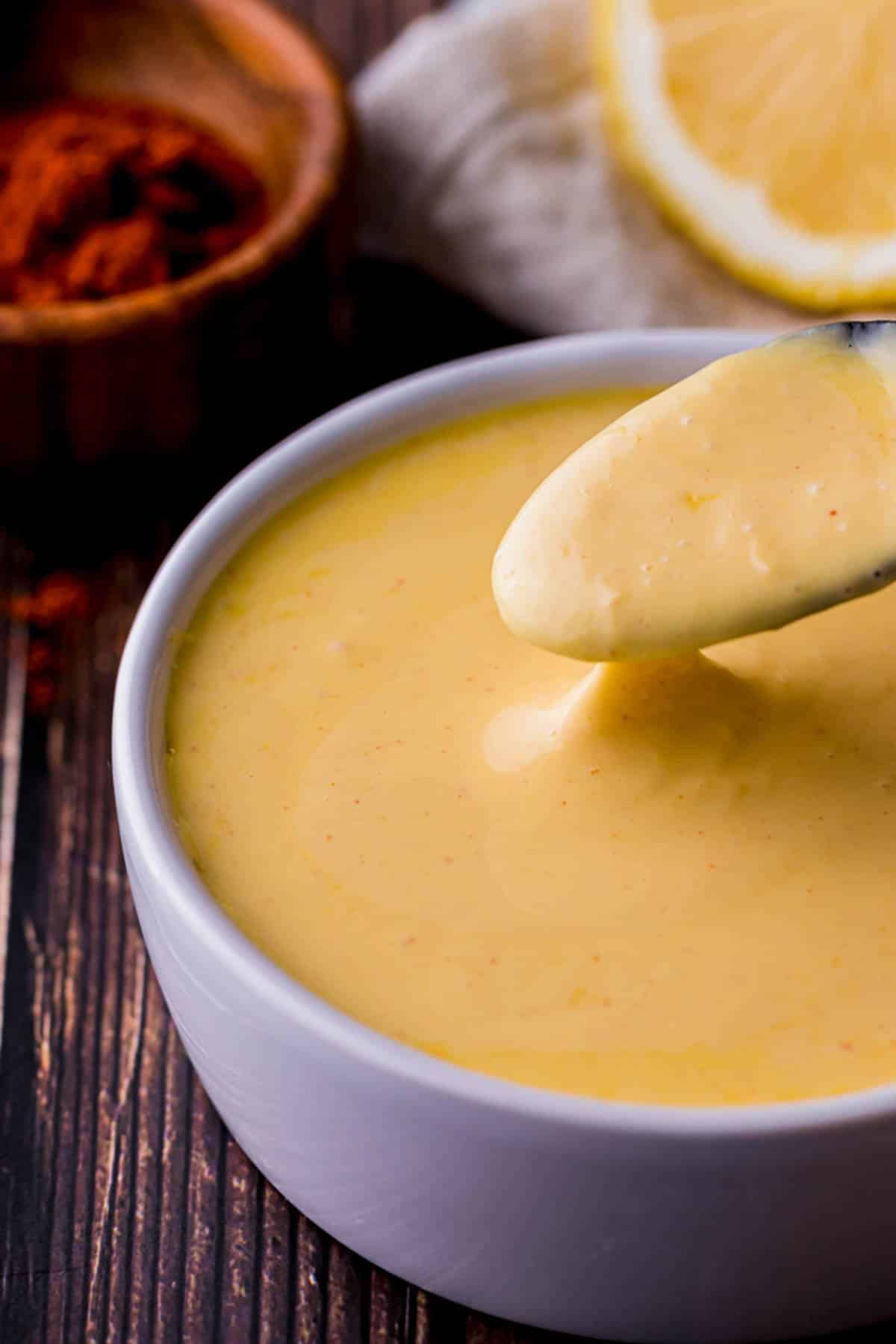 a spoon scooping up hollandaise sauce from a bowl