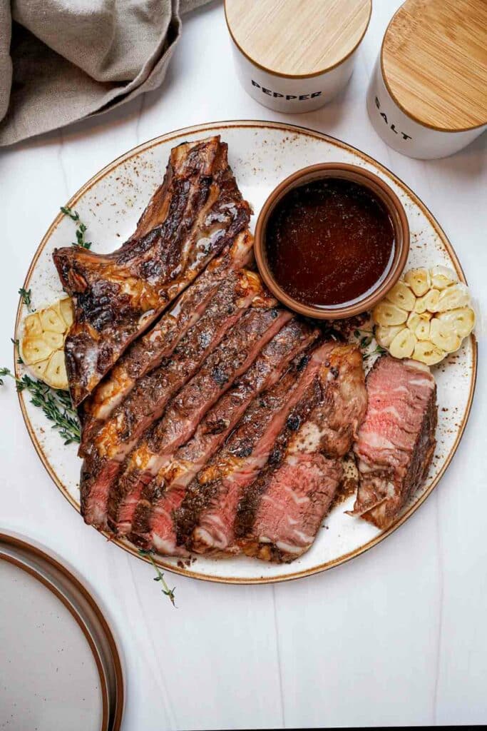 sliced rare beef on a plate with brown sauce on the side