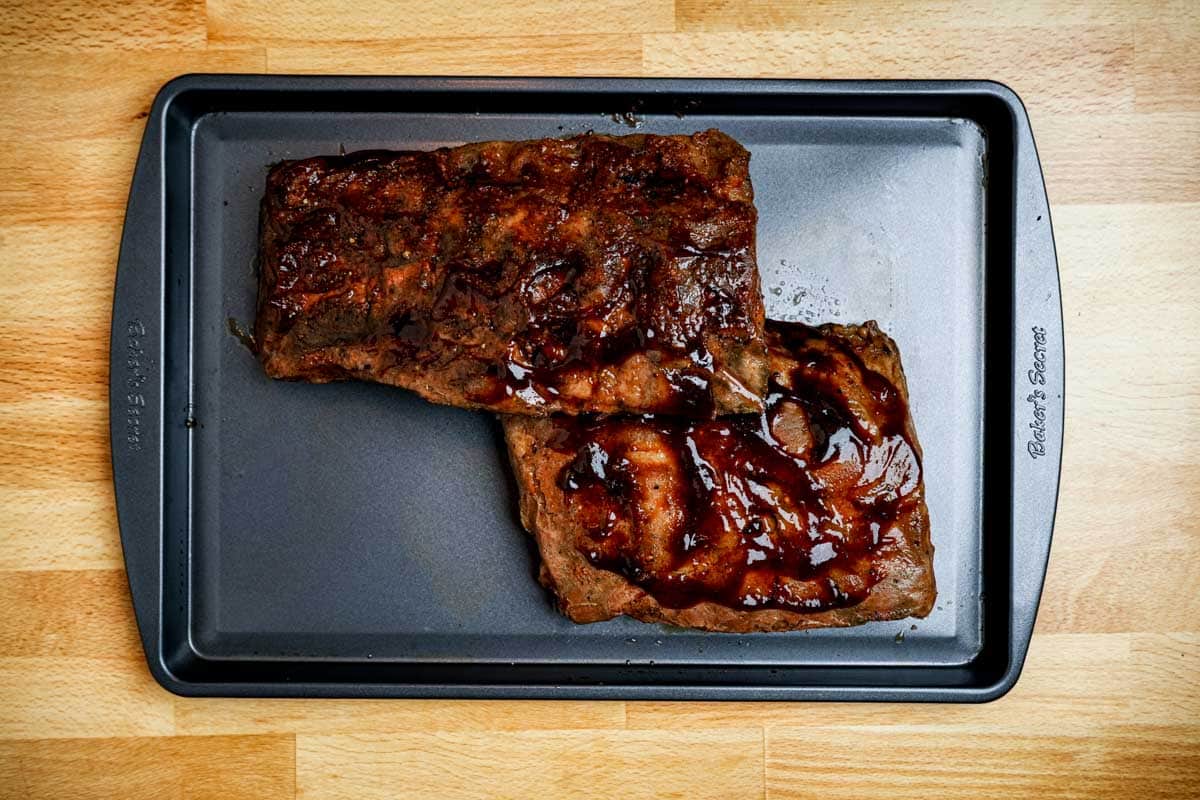 cooked ribs covered with sauce on a baking sheet