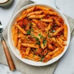 a bowl of penne pasta in red sauce with fork on the side