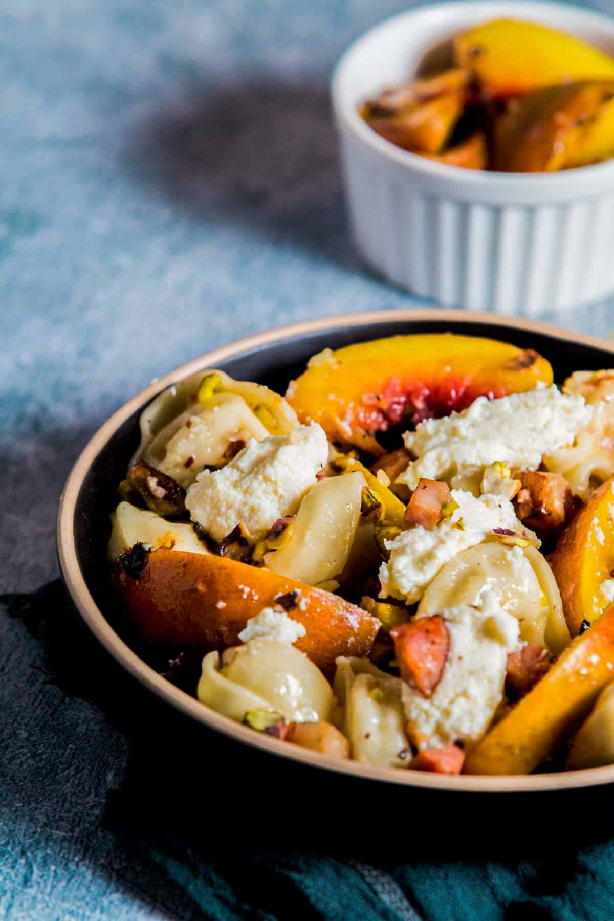 a bowl of tortellini salad with grilled peaches and ricotta cheese