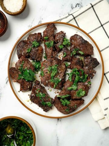 Slices of beef heart on a plate with green herbs