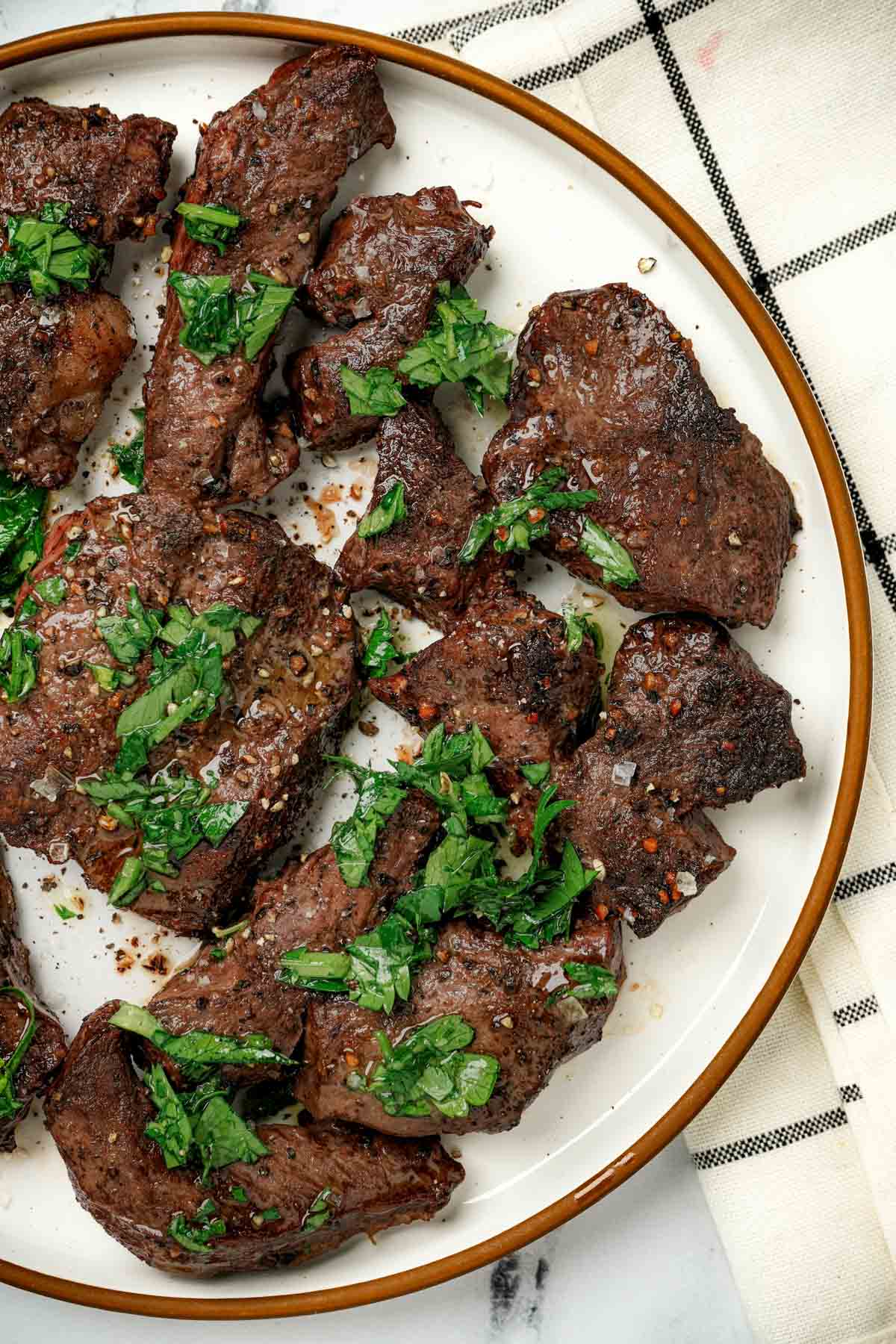 Pieces of beef on a plate with green herb sauce