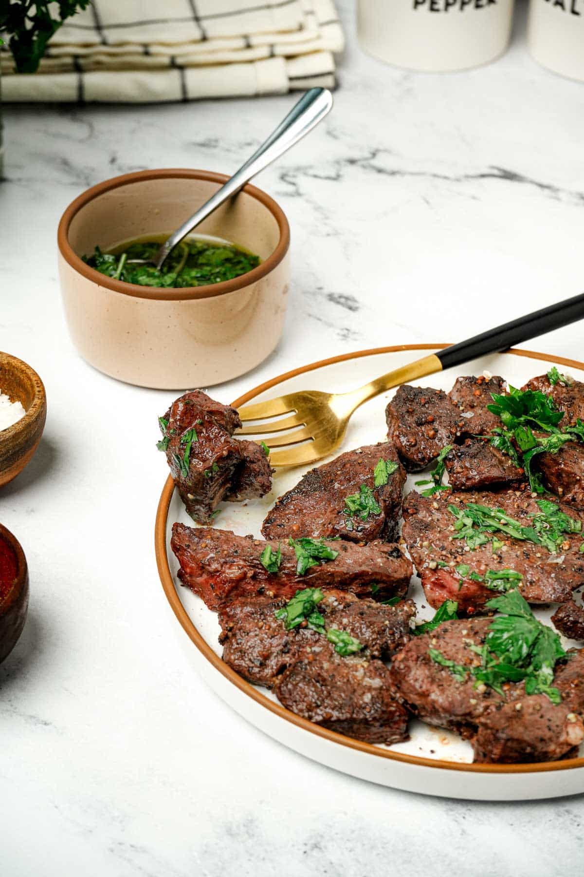 beef heart on a late with a fork garnished with fresh green herbs