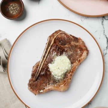 a steak with butter on top on a white plate