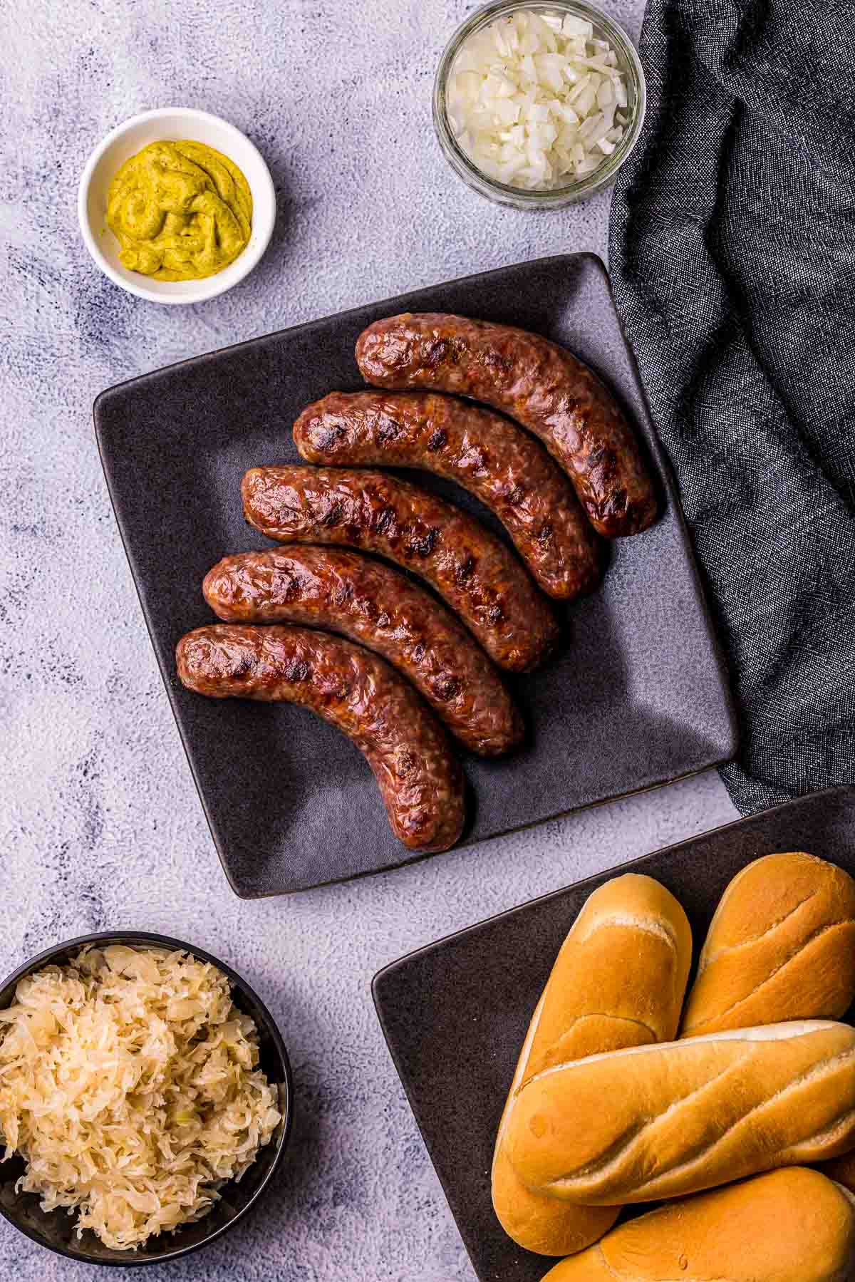 a plate of grilled sausages with buns, mustard and sauerkraut on the side