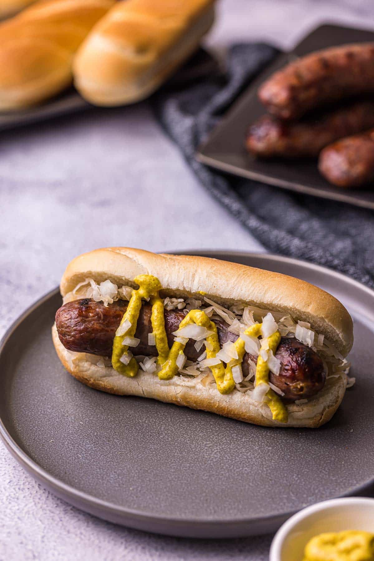 sausage on a bun with mustard and onions on a black plate