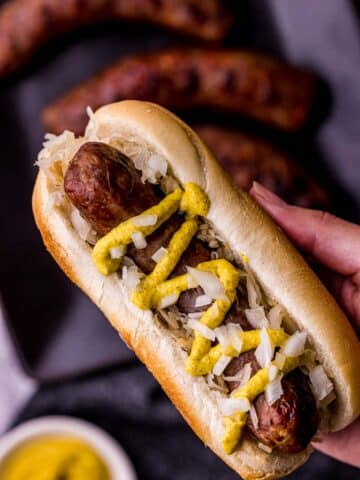 a hand holding a sausage on a bun with mustard and onions