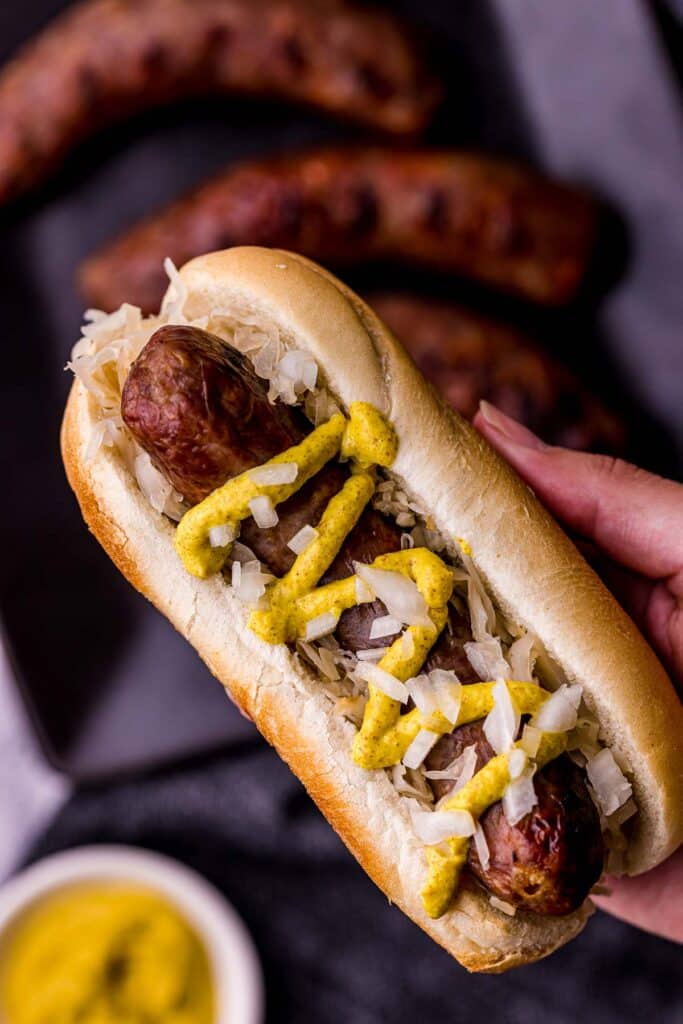 a hand holding a sausage on a bun with mustard and onions