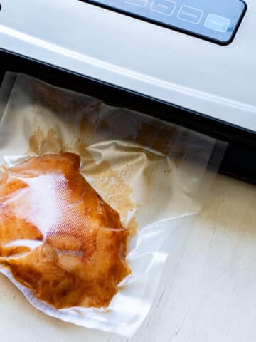 hands putting a bag of chicken into a vacuum sealer