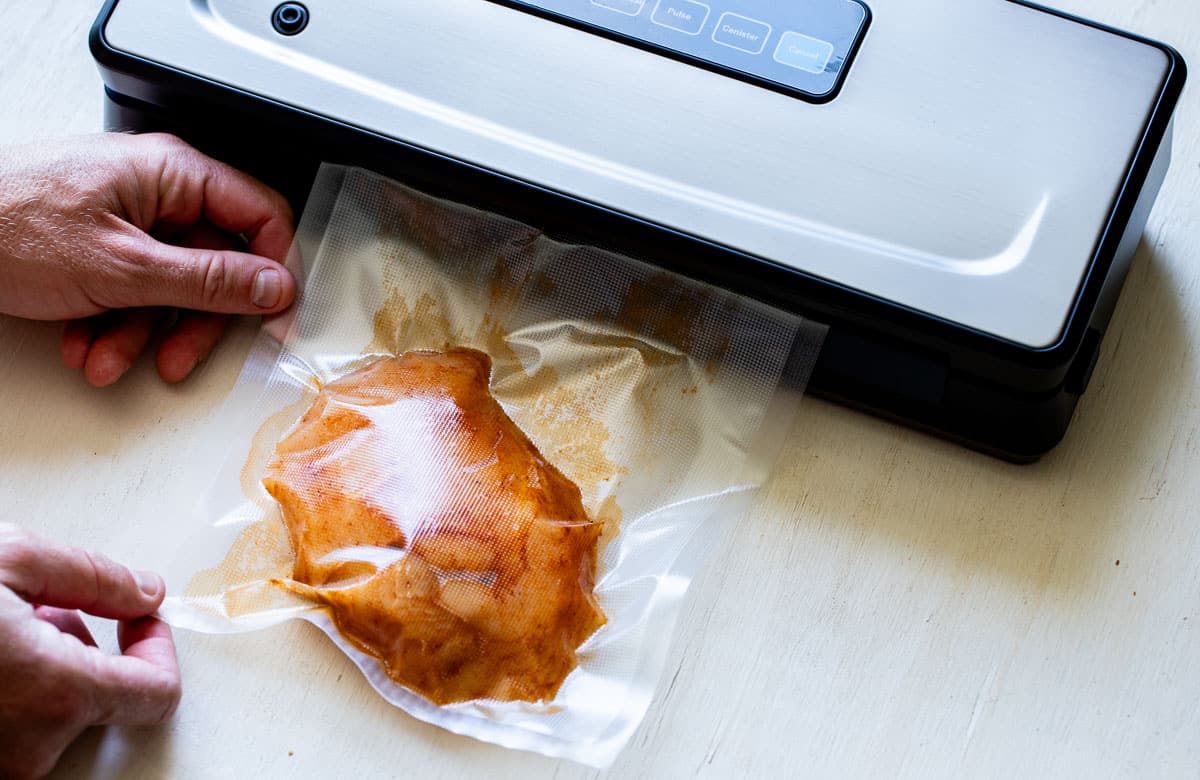 hands putting a bag of chicken into a vacuum sealer